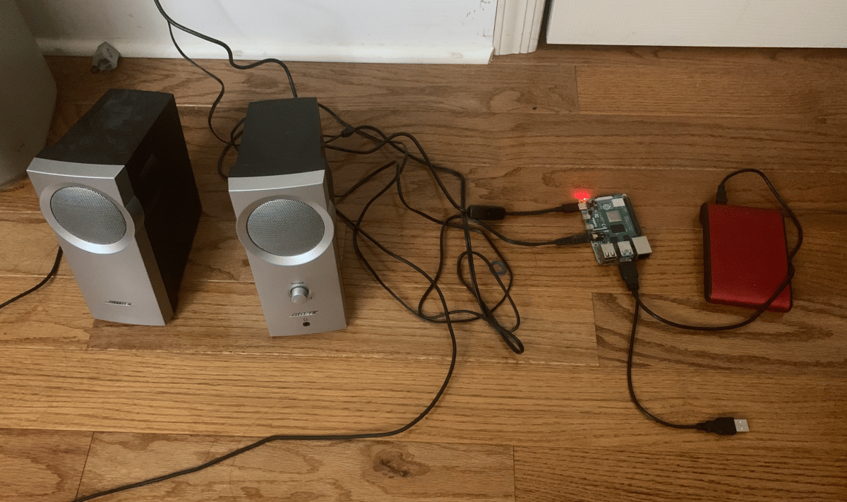 A Raspberry Pi computer attached to an external hard drive and a pair of speakers on the floor.